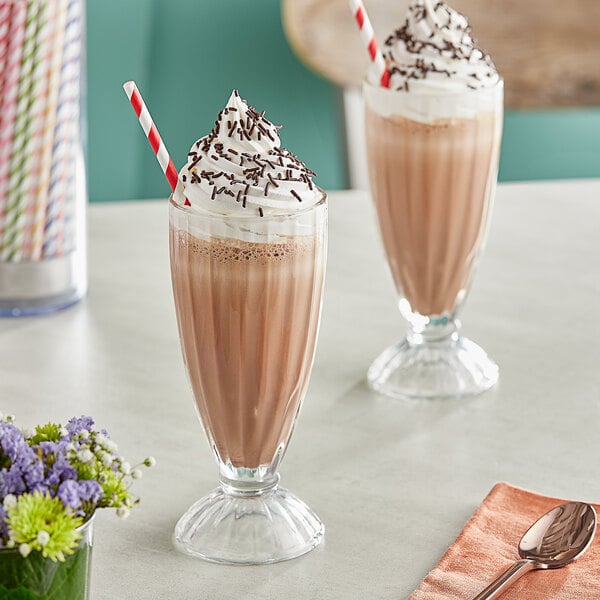 Two glasses of Oringer chocolate milkshakes with whipped cream and chocolate sprinkles on a table.