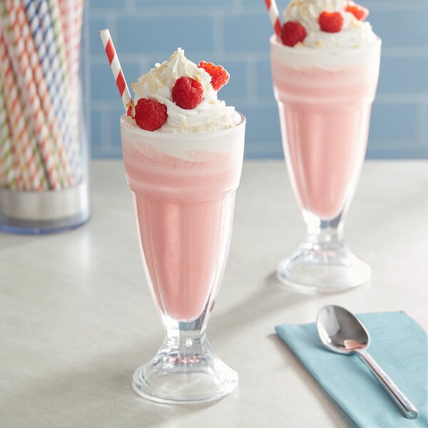 Two glasses of pink milkshakes made with Oringer Raspberry Milkshake Base Syrup and topped with raspberries.