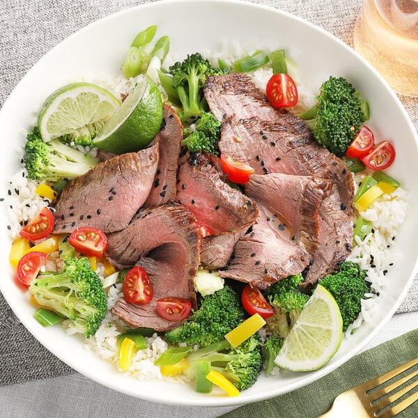 A bowl of rice topped with beef, broccoli, and tomatoes with a lime on the side.