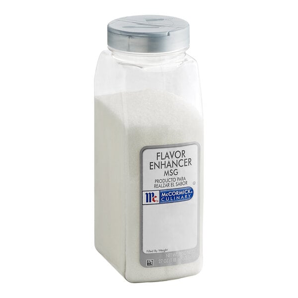 A clear plastic container with a silver lid, filled with a white granular substance and labeled as a flavor enhancer (MSG).