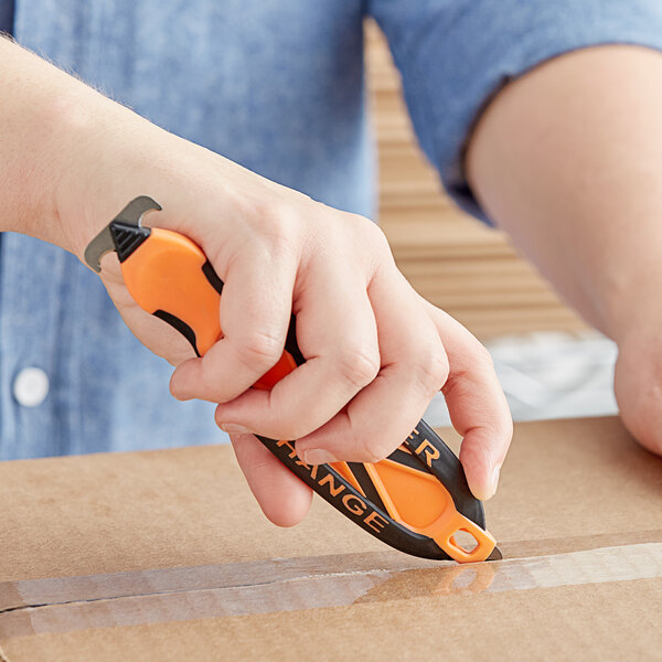 Hand using an orange safety cutter to open a box