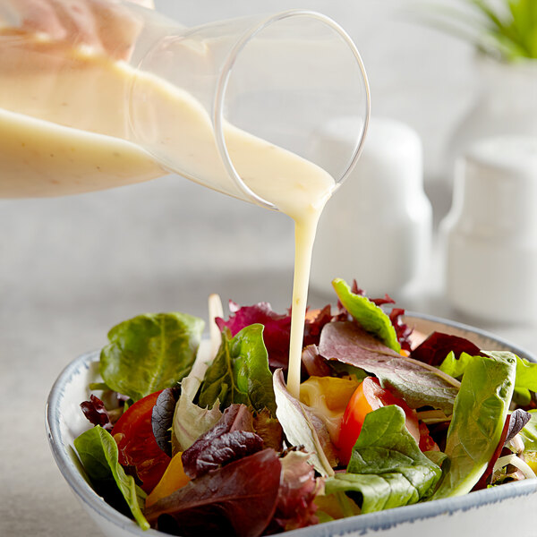 A person pouring AAK Select Recipe Golden Italian Dressing into a bowl of salad.