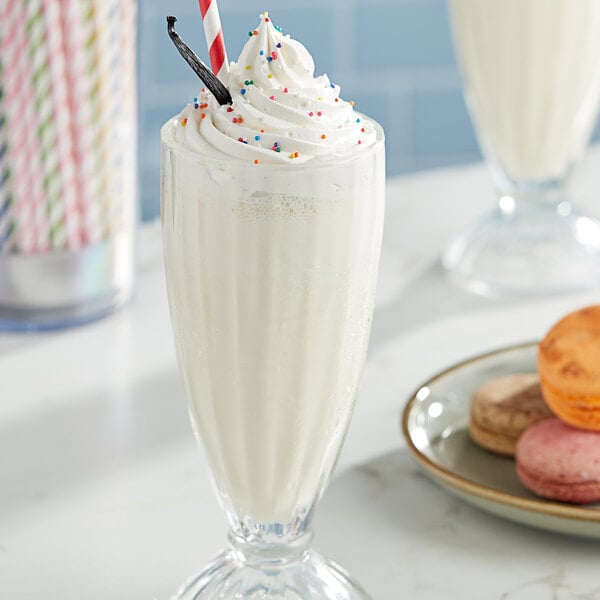 A glass of Oringer vanilla milkshake with sprinkles on top and a cookie on the side.