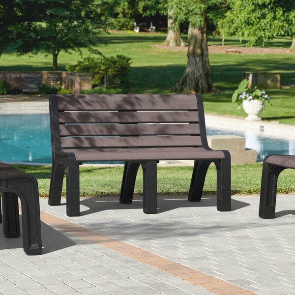 A set of brown Malibu-style benches with black legs on a sidewalk with grass.