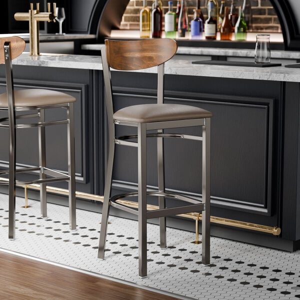 Two Lancaster Table & Seating Boomerang bar stools with taupe vinyl seats and vintage wood backs at a bar counter.