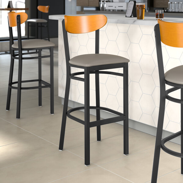 A group of Lancaster Table & Seating Boomerang Series bar stools with cherry wood backs and dark gray vinyl seats at a counter.