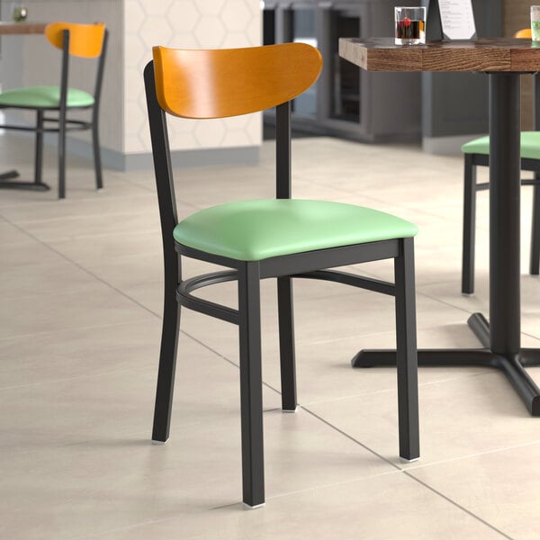 A Lancaster Table & Seating Boomerang chair with a seafoam vinyl seat and cherry wood back on a table in a restaurant