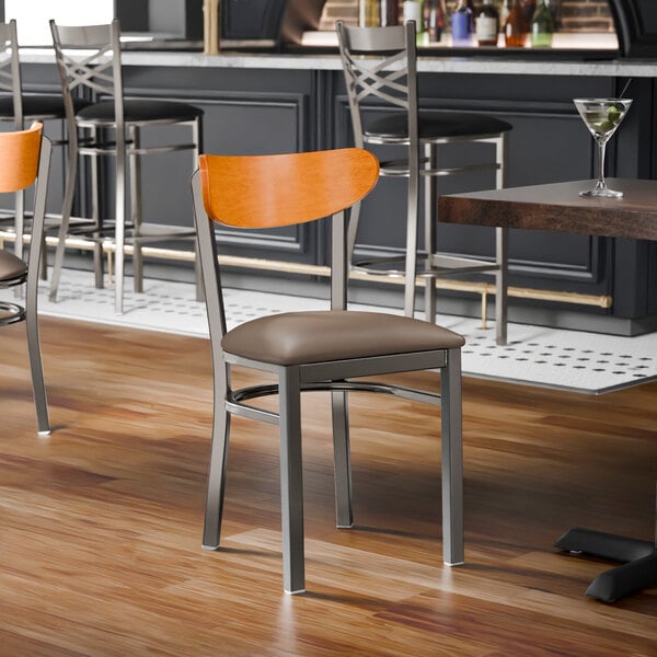 A metal chair with a taupe vinyl seat and a cherry wood backrest, designed for commercial dining settings.
