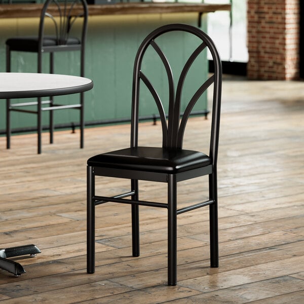 A Lancaster Table & Seating black Spoke Back chair with a black cushion sits in front of a table in a restaurant.
