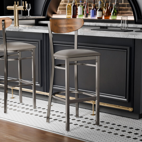 Two Lancaster Table & Seating Boomerang bar stools with a wood back and dark gray vinyl seats at a bar counter.