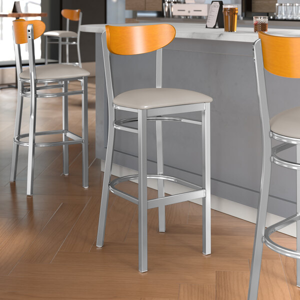 Lancaster Table & Seating Boomerang Series bar stools with light gray vinyl seats and cherry wood backs.