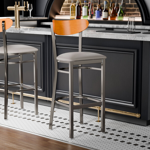 A Lancaster Table & Seating Boomerang bar stool with a light gray vinyl seat and cherry wood back on a counter.