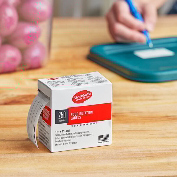 A hand uses a knife to cut a roll of Cambro StoreSafe food rotation labels on a counter.