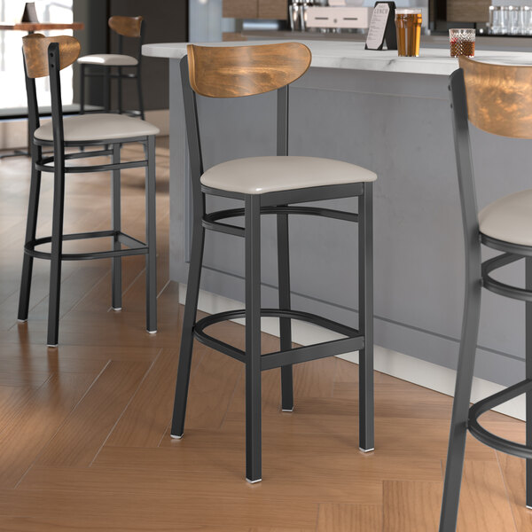 Lancaster Table & Seating black bar stool with wood and white vinyl seat next to a counter.