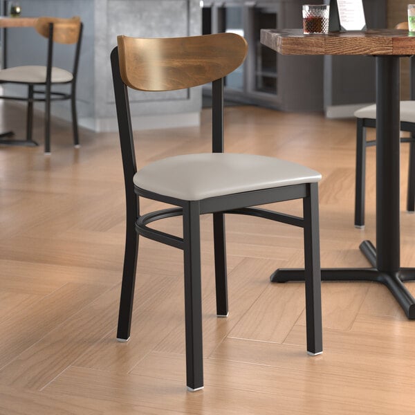 A Lancaster Table & Seating Boomerang Series chair with a wood back and light gray seat at a table in a restaurant.