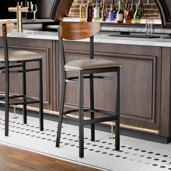 A black bar stool with a taupe vinyl seat and a curved vintage wood backrest.