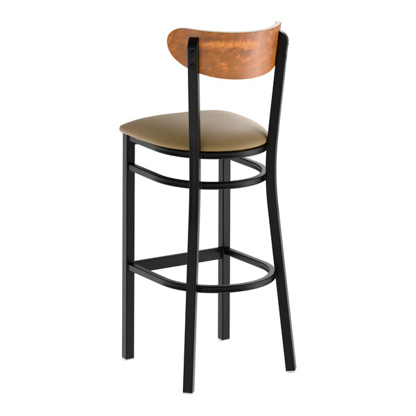 A bar stool with a black metal frame, taupe vinyl seat, and a curved vintage wood backrest.