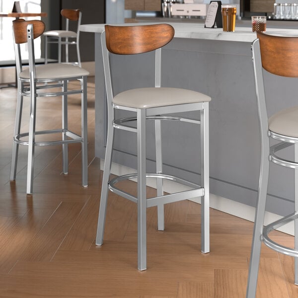 Lancaster Table & Seating bar stools with wooden backs and light gray vinyl seats.