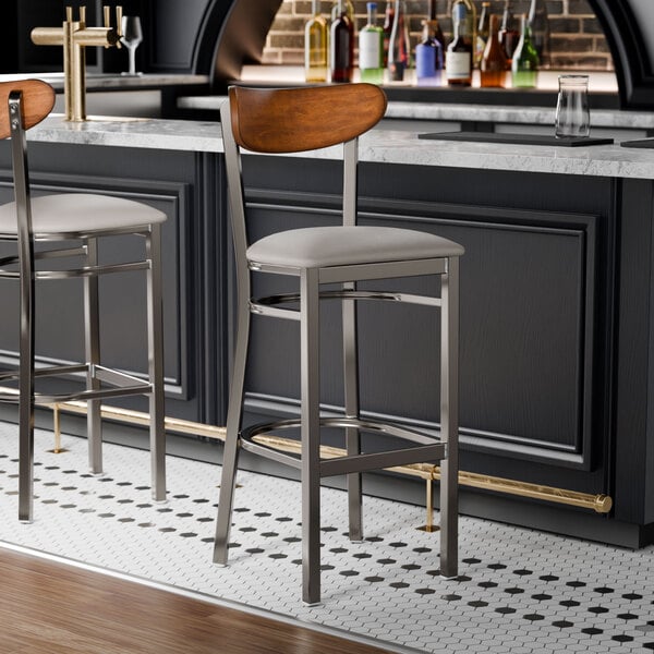 Two Lancaster Table & Seating bar stools with a light gray cushion at a bar counter.