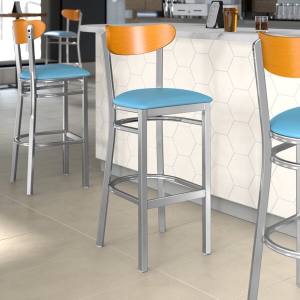 A group of Lancaster Table & Seating Boomerang Series bar stools with blue vinyl seats and cherry wood backs.