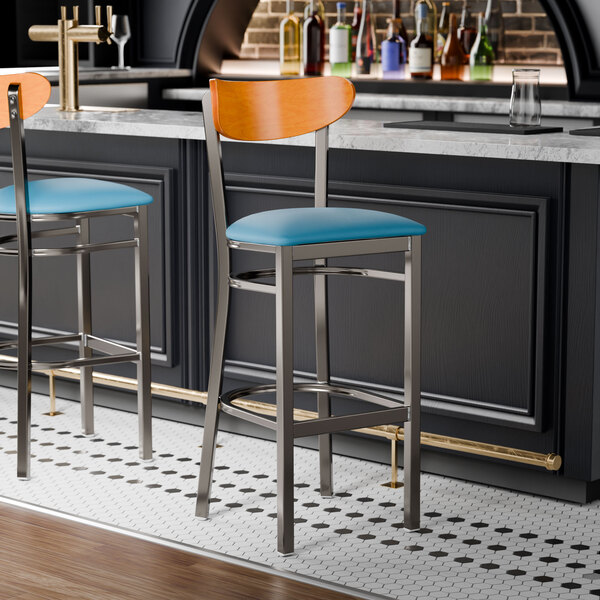 Two Lancaster Table & Seating bar stools with blue seats and cherry wood backs at a black counter.