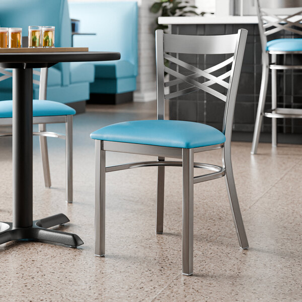 A metal chair with a cross back design and a blue vinyl padded seat.