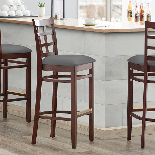 Three Lancaster Table & Seating mahogany wood bar stools with dark gray vinyl seats and window backs.