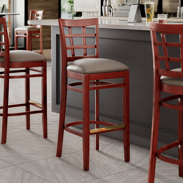 Three Lancaster Table & Seating mahogany wood bar stools with dark gray vinyl seats.
