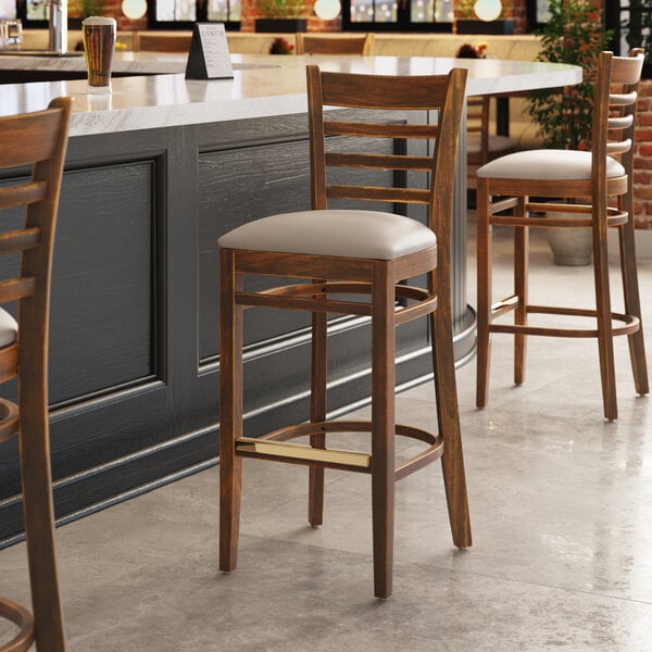 A Lancaster Table & Seating wooden ladder back bar stool with a light gray cushion on a white table next to a counter.