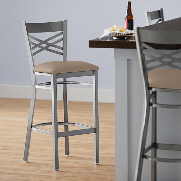 A Lancaster Table & Seating cross back bar stool with a detached taupe vinyl padded seat.