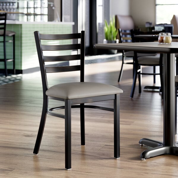 A metal ladder back chair with a dark gray vinyl padded seat and a distressed copper finish.