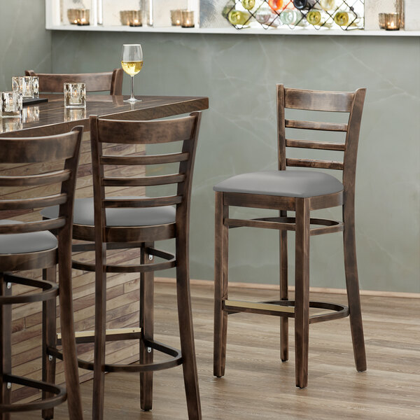 A Lancaster Table & Seating wooden ladder back bar stool with a light gray cushion on the seat at a table in a restaurant.