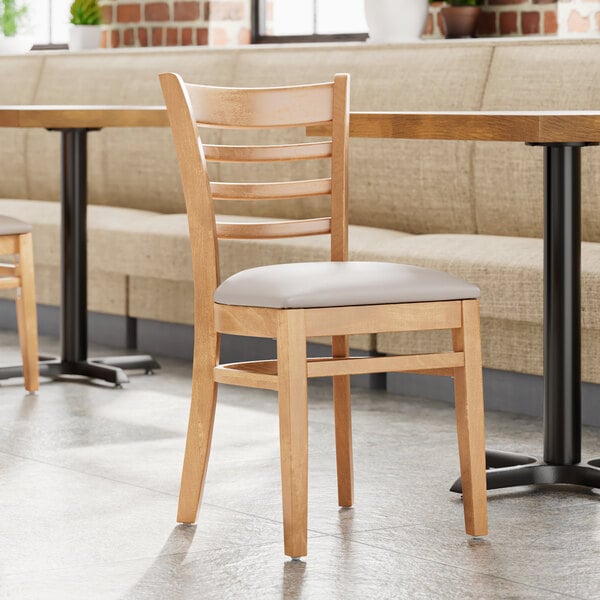 A Lancaster Table & Seating wooden ladder back chair with a light gray vinyl seat.