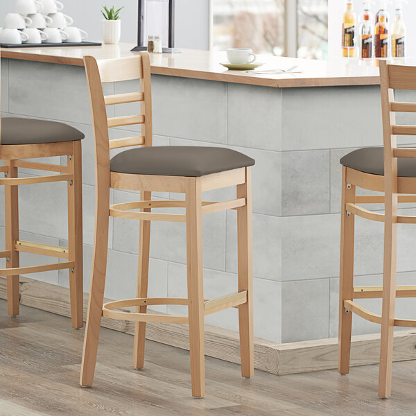 Three Lancaster Table & Seating wood ladder back bar stools with taupe vinyl seats at a kitchen counter.