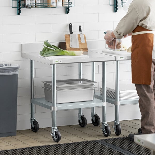 A man in an apron standing next to a Regency stainless steel work table with casters.