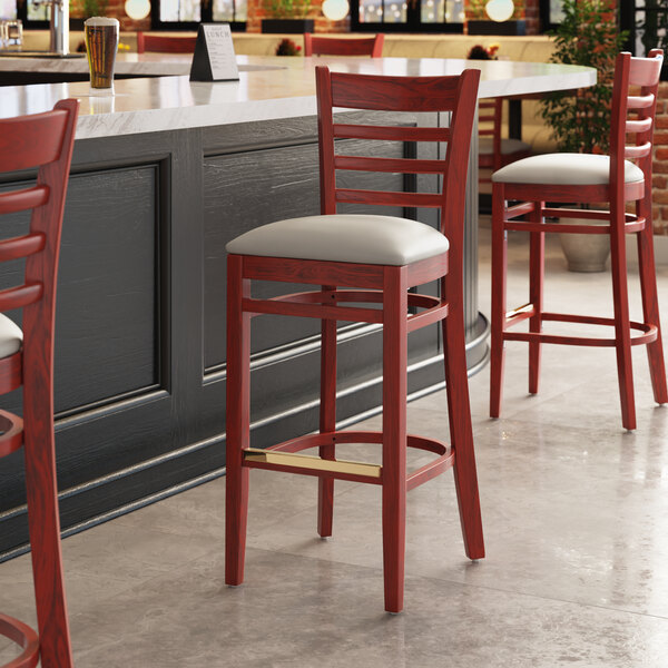 A Lancaster Table & Seating mahogany wood ladder back bar stool with a dark gray vinyl seat next to a counter.