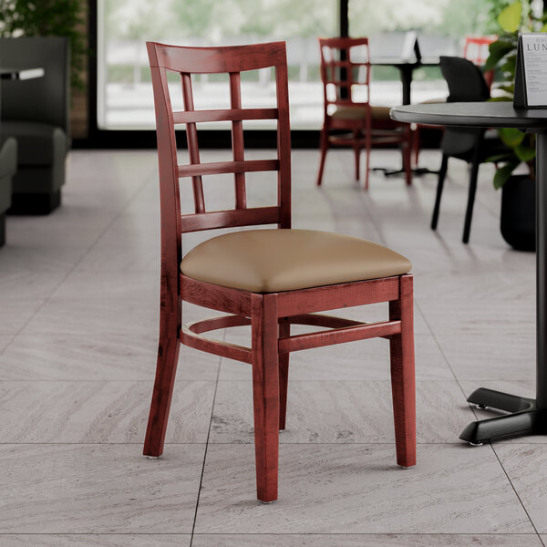 A Lancaster Table & Seating wooden chair with a taupe vinyl seat in a restaurant.