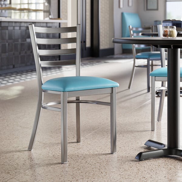 A Lancaster Table & Seating black metal ladder back chair with a blue vinyl cushion on a table.