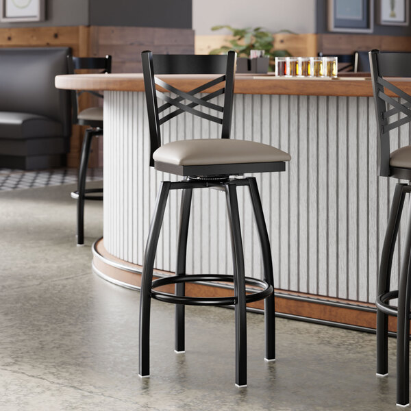 A black metal bar stool with a cross back design and a light gray vinyl padded swivel seat.
