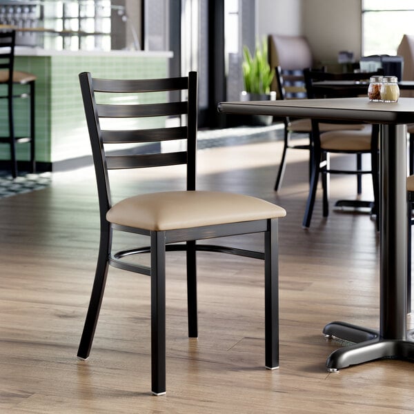 A ladder back chair with a distressed copper finish and a taupe vinyl padded seat.