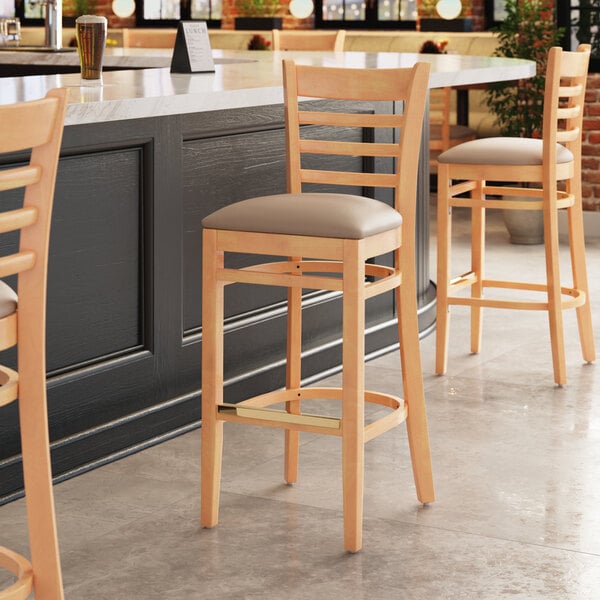 A Lancaster Table & Seating wooden ladder back bar stool with a taupe vinyl seat.