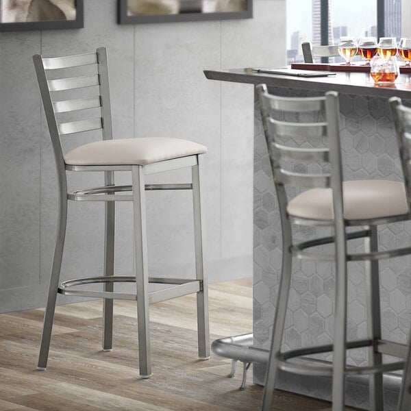 A Lancaster Table & Seating clear coat finish ladder back bar stool with a light gray vinyl padded seat.