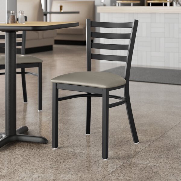 A Lancaster Table & Seating black ladder back chair with dark gray vinyl cushion on a table in a restaurant.