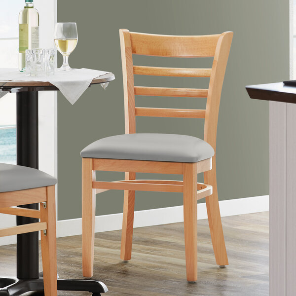 A Lancaster Table & Seating wooden ladder back chair with a light gray vinyl seat.