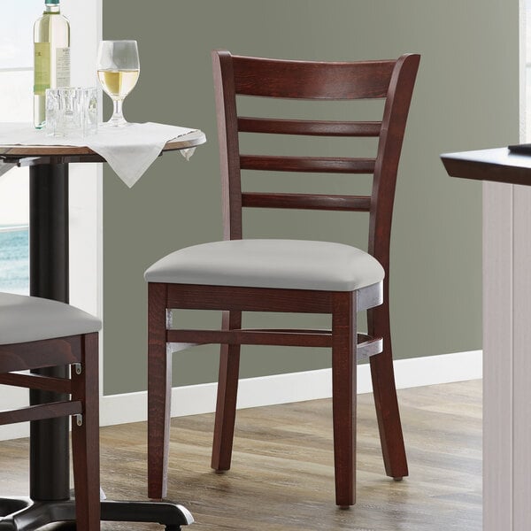 A Lancaster Table & Seating mahogany wood chair with a light gray vinyl seat next to a table in a restaurant.