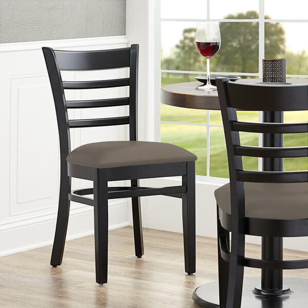 A close-up of a Lancaster Table & Seating black wood ladder back chair with a taupe vinyl seat.