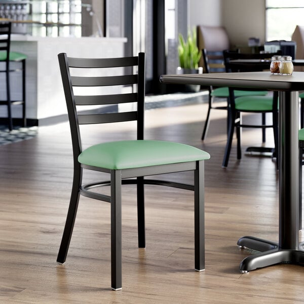 A black ladder back chair with a seafoam green vinyl padded seat.