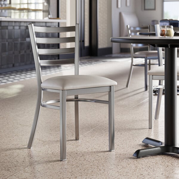 A Lancaster Table & Seating clear coat finish ladder back chair with a light gray vinyl padded seat.