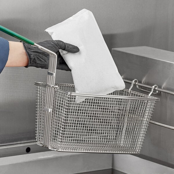 A person in black gloves using a green FreshFry filtration pod tool to lift a basket of oil.