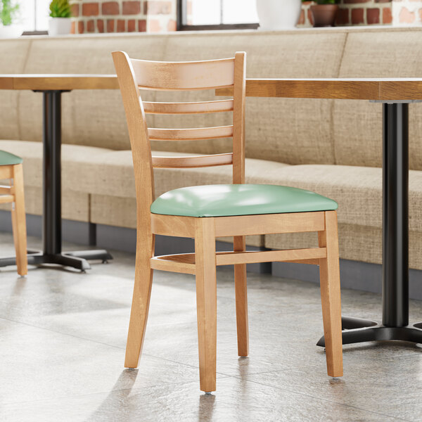 A Lancaster Table & Seating wooden chair with a seafoam vinyl seat in a restaurant.